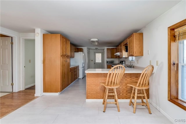 kitchen featuring kitchen peninsula, white fridge, a breakfast bar area, and sink