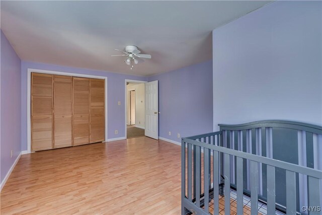 bedroom featuring a nursery area, a closet, light hardwood / wood-style flooring, and ceiling fan