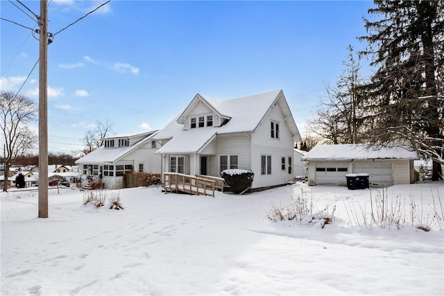 snow covered property featuring a garage, an outbuilding, and a wooden deck