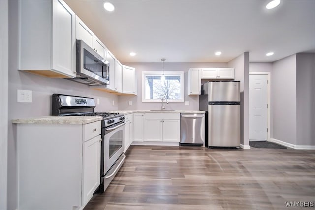 kitchen with stainless steel appliances, sink, white cabinetry, hanging light fixtures, and dark wood-type flooring