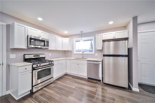 kitchen featuring stainless steel appliances, hanging light fixtures, light stone counters, white cabinets, and sink