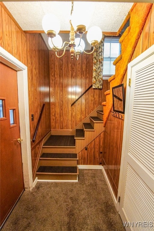 stairway featuring wooden walls, an inviting chandelier, and carpet flooring