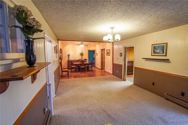 interior space featuring carpet floors, wooden walls, a textured ceiling, baseboard heating, and ceiling fan with notable chandelier