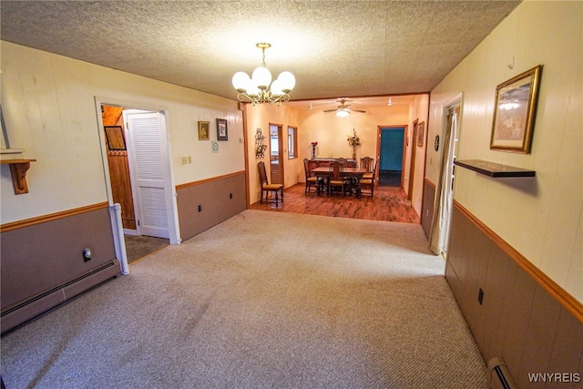 carpeted dining space featuring ceiling fan with notable chandelier, a textured ceiling, a baseboard heating unit, and wood walls