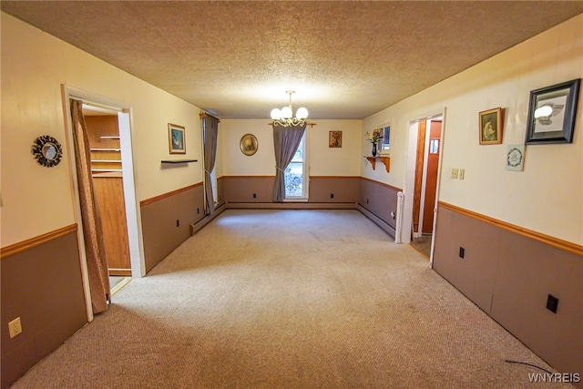 empty room featuring light colored carpet, a textured ceiling, baseboard heating, and a notable chandelier