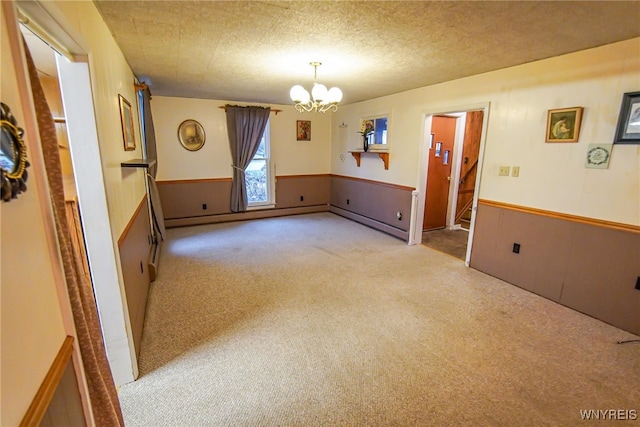 empty room with light colored carpet, a baseboard radiator, a chandelier, and a textured ceiling