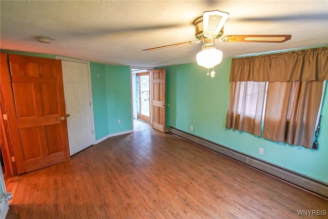 empty room with ceiling fan, a baseboard heating unit, and hardwood / wood-style flooring