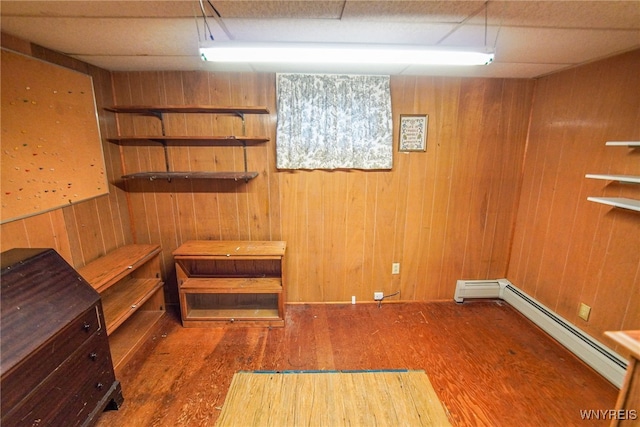 interior space with dark wood-type flooring, a drop ceiling, a baseboard heating unit, and wood walls