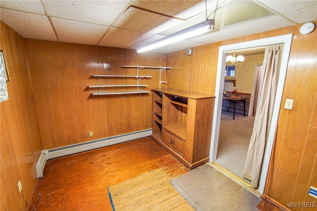 basement with baseboard heating, a chandelier, a paneled ceiling, and wooden walls