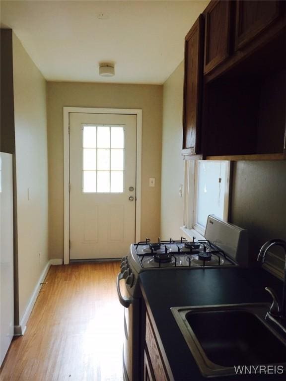 kitchen with sink, light hardwood / wood-style floors, white fridge, dark brown cabinetry, and range with gas cooktop