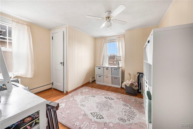 bedroom featuring a baseboard heating unit, light hardwood / wood-style floors, a textured ceiling, and ceiling fan