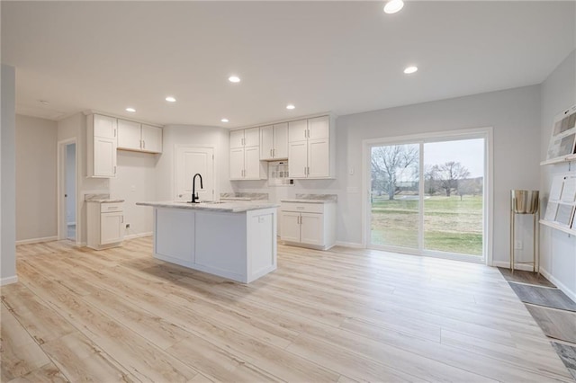 kitchen with white cabinets, sink, light wood-type flooring, and a kitchen island with sink