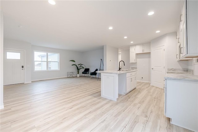 kitchen with a center island with sink, light stone countertops, white cabinetry, and light wood-type flooring