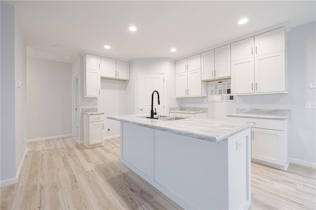 kitchen featuring white cabinets, a center island with sink, light hardwood / wood-style floors, and sink