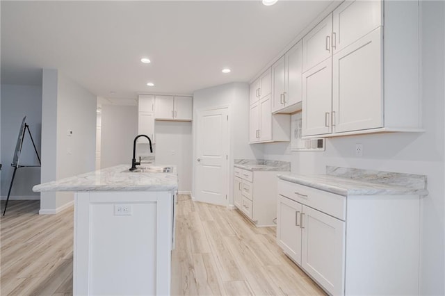 kitchen featuring a kitchen island with sink, white cabinets, sink, light wood-type flooring, and light stone counters