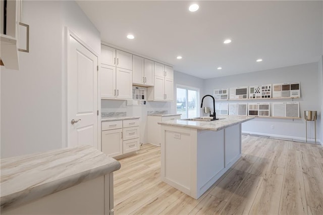 kitchen featuring white cabinets, sink, light wood-type flooring, and a kitchen island with sink