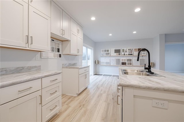 kitchen featuring white cabinets, sink, a kitchen island, light stone countertops, and light hardwood / wood-style floors