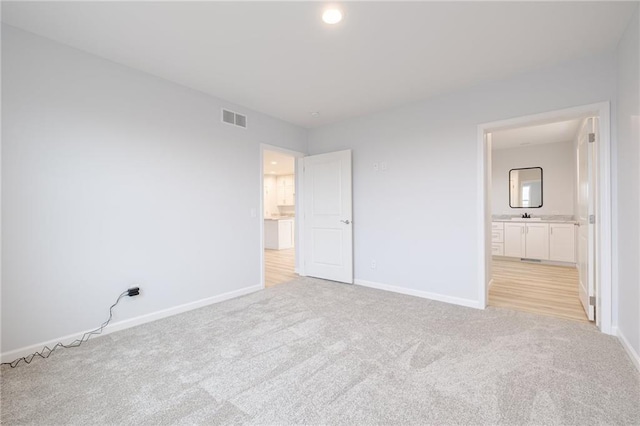 unfurnished bedroom featuring sink, light carpet, and connected bathroom