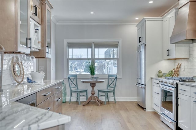 kitchen featuring high end appliances, white cabinets, light stone counters, and wall chimney exhaust hood