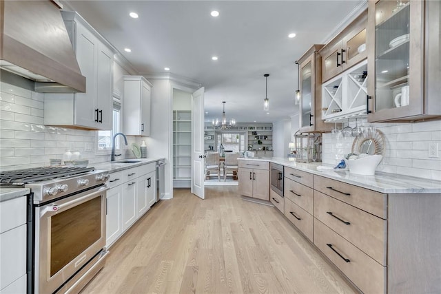 kitchen with white cabinets, decorative light fixtures, stainless steel appliances, and wall chimney exhaust hood