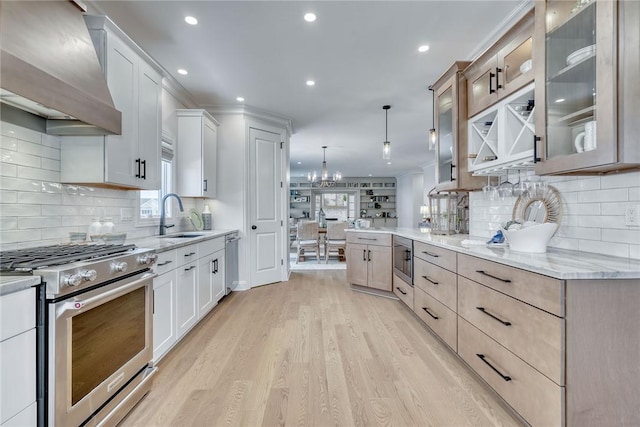 kitchen with wall chimney range hood, hanging light fixtures, white cabinets, and appliances with stainless steel finishes