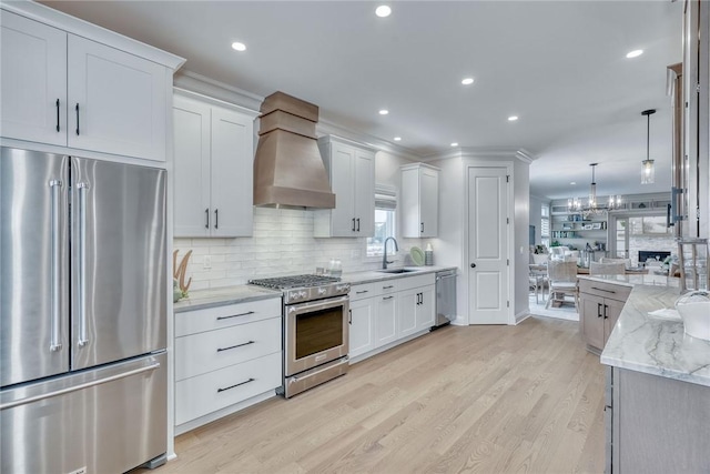 kitchen with sink, premium range hood, high quality appliances, white cabinets, and decorative light fixtures