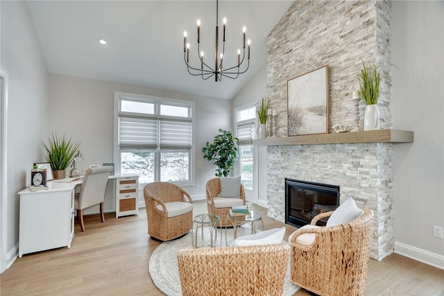 living room with high vaulted ceiling, a stone fireplace, light hardwood / wood-style floors, and a chandelier