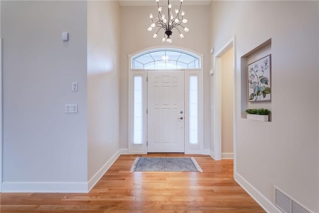 foyer entrance with light hardwood / wood-style floors, a high ceiling, and an inviting chandelier