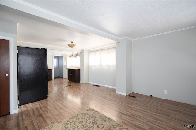 unfurnished living room with hardwood / wood-style floors, an inviting chandelier, a textured ceiling, and ornamental molding