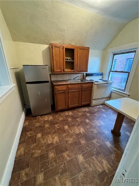 kitchen with stainless steel refrigerator, sink, white range with electric stovetop, a textured ceiling, and lofted ceiling