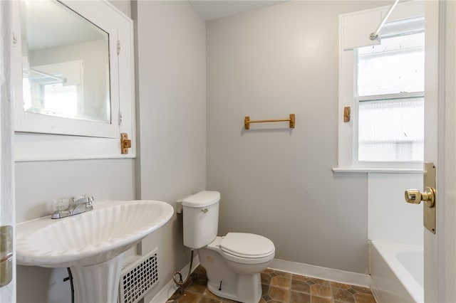 bathroom with tile patterned flooring, a tub to relax in, toilet, and a wealth of natural light