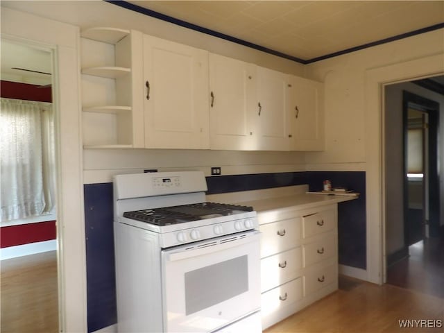 kitchen featuring white cabinets, ornamental molding, light hardwood / wood-style flooring, and gas range gas stove