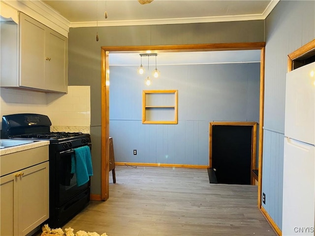 kitchen featuring pendant lighting, crown molding, light hardwood / wood-style floors, black gas range oven, and white fridge