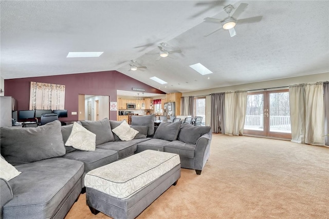 living room featuring light colored carpet, ceiling fan, french doors, vaulted ceiling with skylight, and a textured ceiling