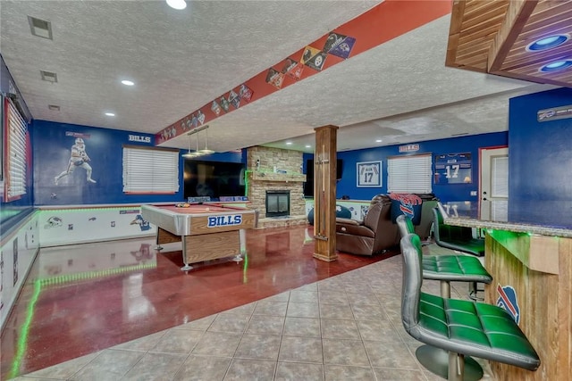 playroom with a textured ceiling, a stone fireplace, light tile patterned flooring, and decorative columns