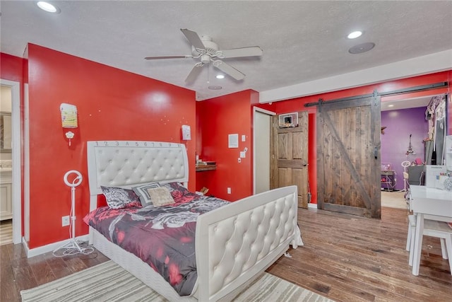 bedroom featuring ceiling fan, a barn door, a textured ceiling, and wood-type flooring