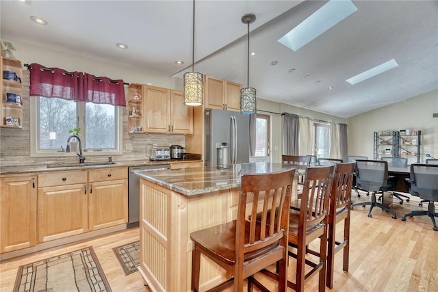 kitchen featuring a center island, lofted ceiling with skylight, tasteful backsplash, appliances with stainless steel finishes, and sink