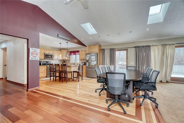 dining area featuring sink, light hardwood / wood-style floors, vaulted ceiling with skylight, and a wealth of natural light