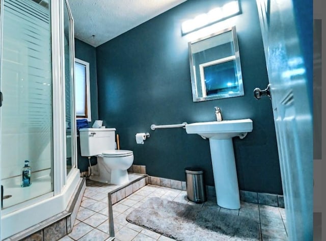 bathroom with toilet, tile patterned floors, a shower with shower door, a textured ceiling, and sink