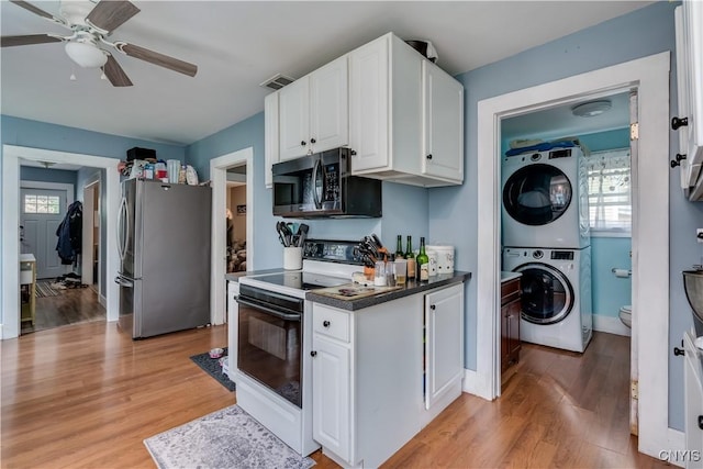 kitchen with white electric range, stacked washing maching and dryer, stainless steel refrigerator, and white cabinetry