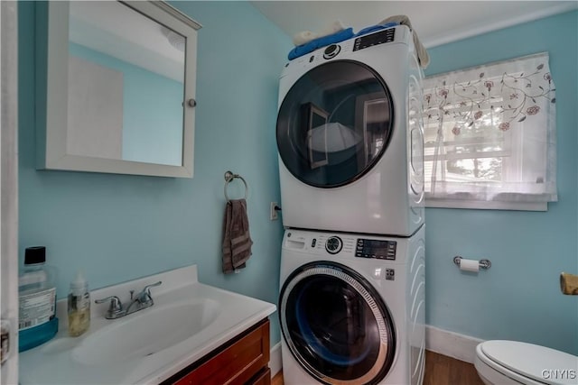 washroom featuring wood-type flooring, stacked washing maching and dryer, and sink