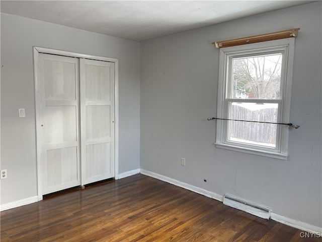 unfurnished bedroom featuring a baseboard heating unit, a closet, and dark hardwood / wood-style floors