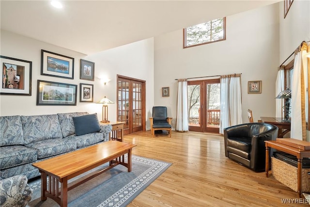 living room featuring light wood-type flooring, a high ceiling, and french doors