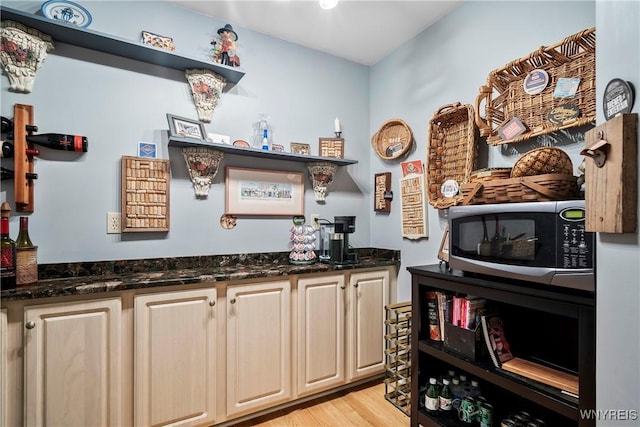 bar with light hardwood / wood-style flooring and dark stone counters