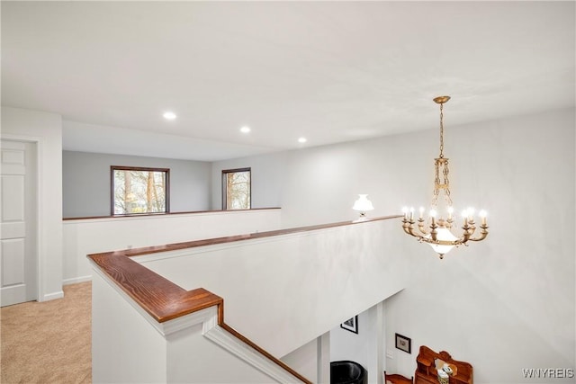 hall featuring light carpet and an inviting chandelier