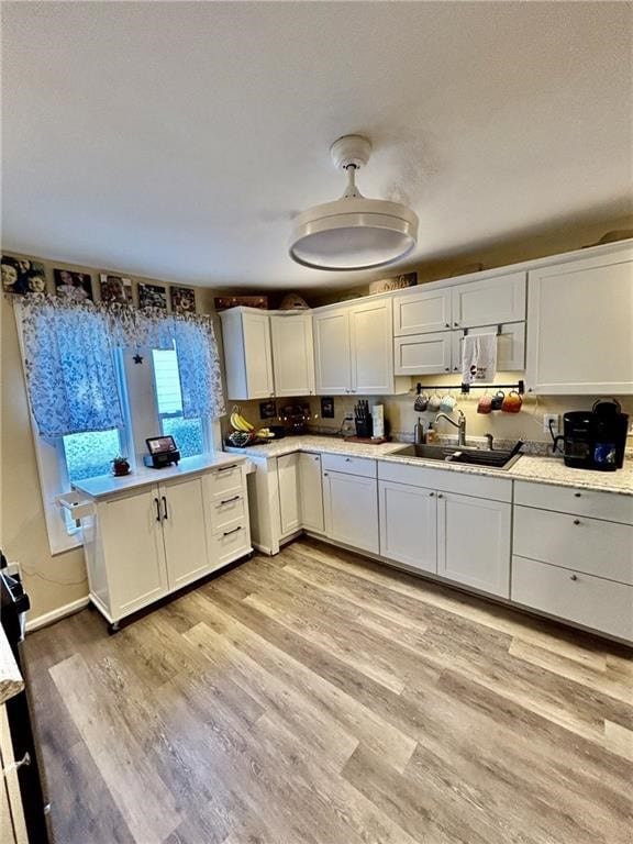 kitchen with white cabinetry, sink, and light hardwood / wood-style flooring