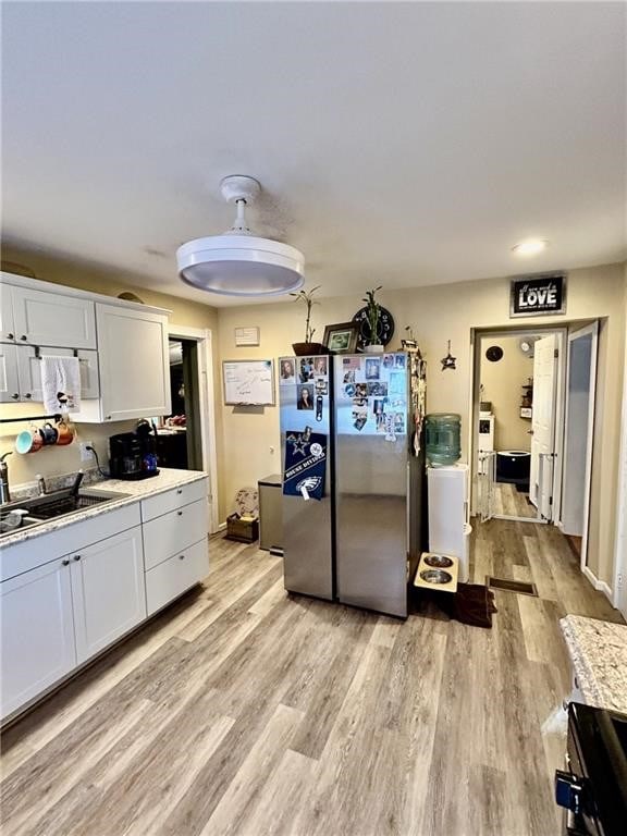 kitchen with stainless steel refrigerator, white cabinetry, sink, stove, and light wood-type flooring