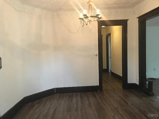 spare room featuring ornamental molding, dark wood-type flooring, and a chandelier