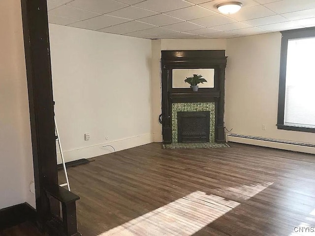 unfurnished living room with a paneled ceiling, dark wood-type flooring, and a baseboard heating unit