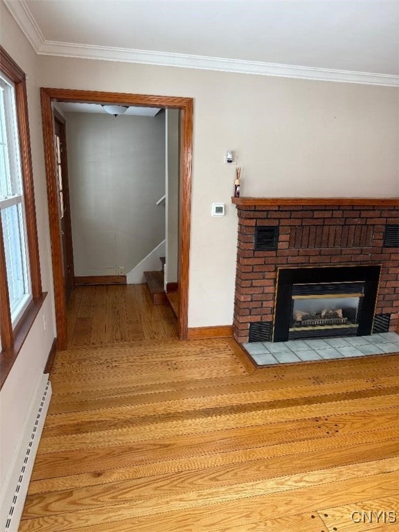 unfurnished living room featuring a brick fireplace, light hardwood / wood-style floors, ornamental molding, and a baseboard radiator